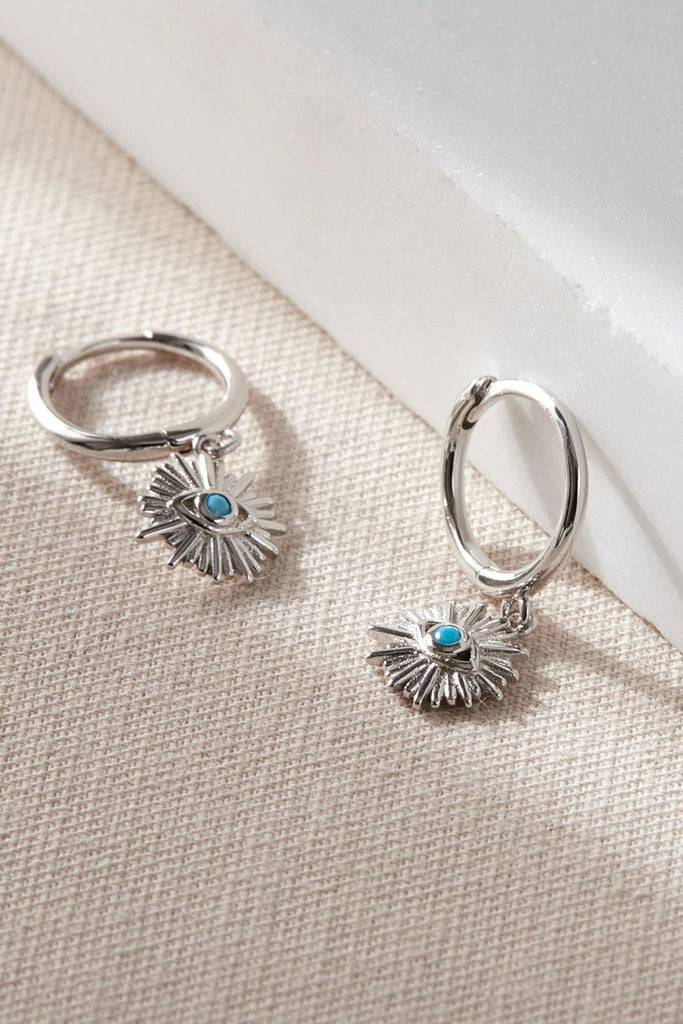 close up of the silver coloured evil eye charm earrings, showing a close up of the blue eye surrounded by sun rays