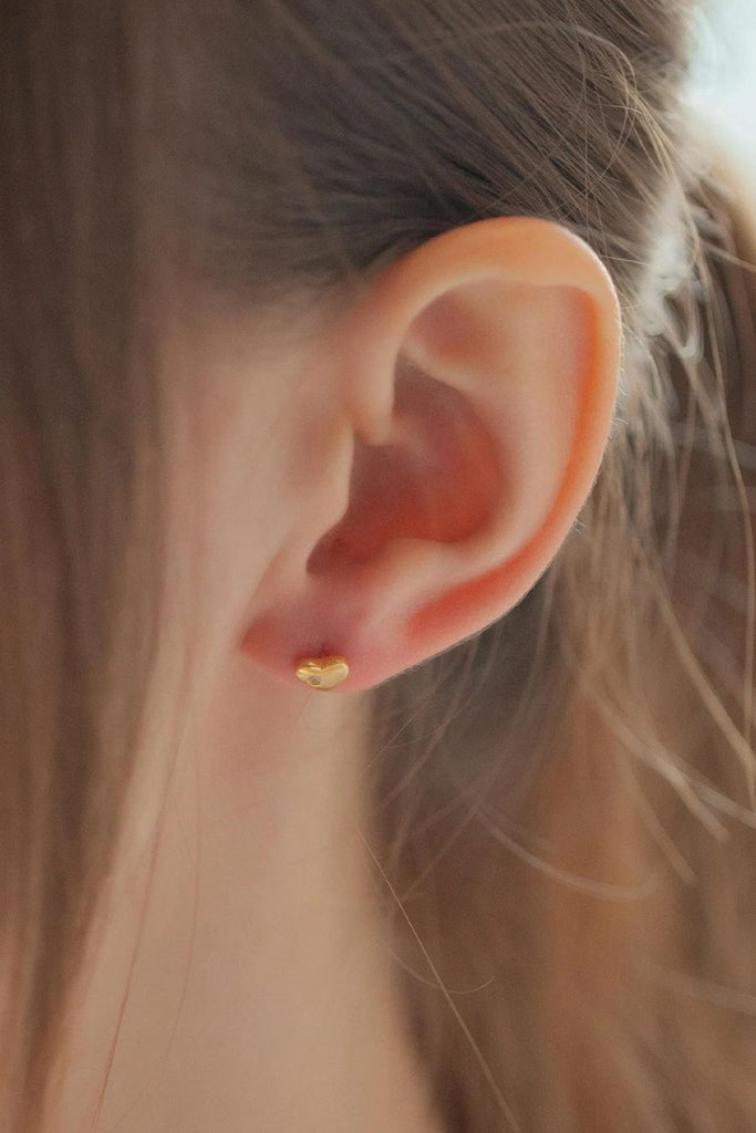 model wearing a small gold love heart stud earring on the earlobe showing the dainty size of the jewellery