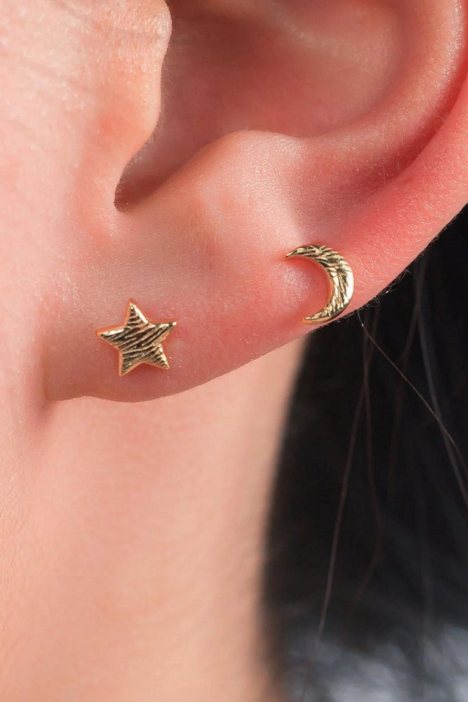 model wearing both the gold star and moon studs on the earlobe showing that these can be worn as stacking earrings, the textured surface of the studs is visible