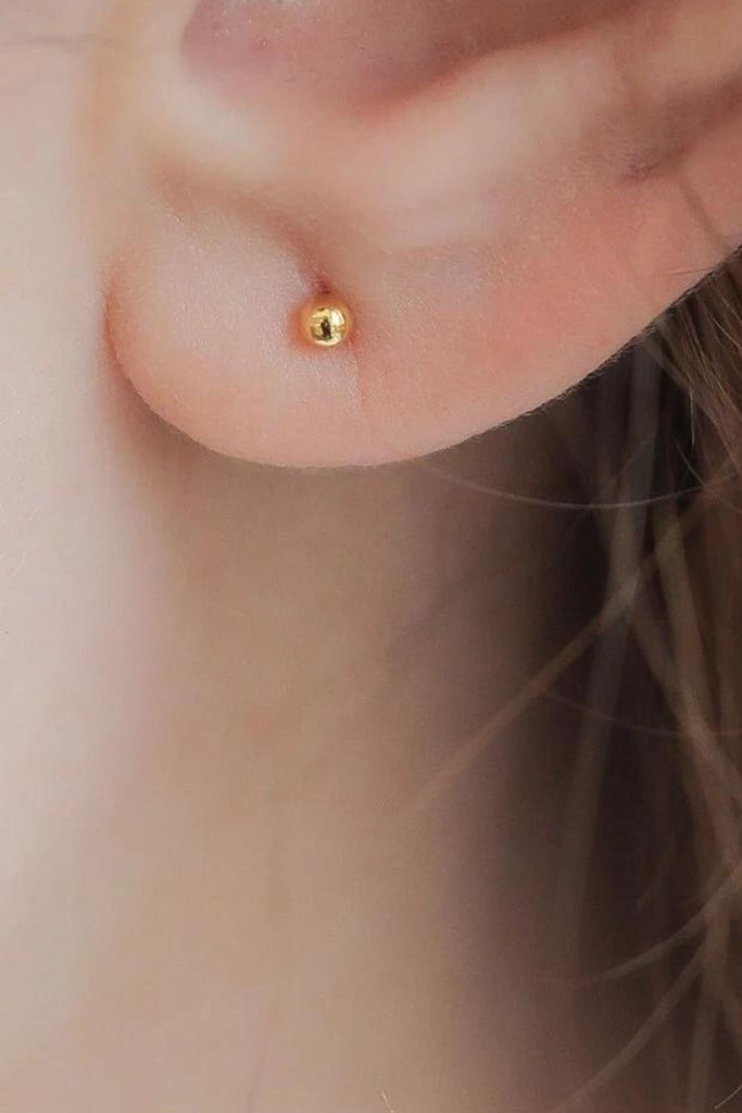 model wearing a small round smooth stud earring on the earlobe showing the dainty size of the earrings