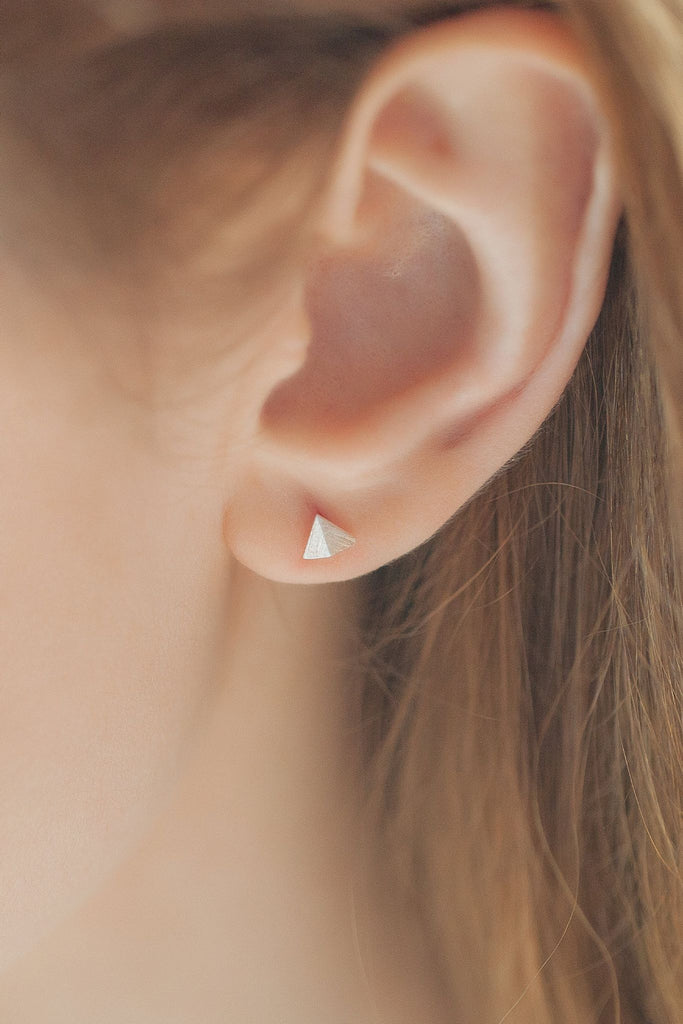 model wearing a sterling silver pyramid stud earring in the earlobe showing the dainty size of the earrings