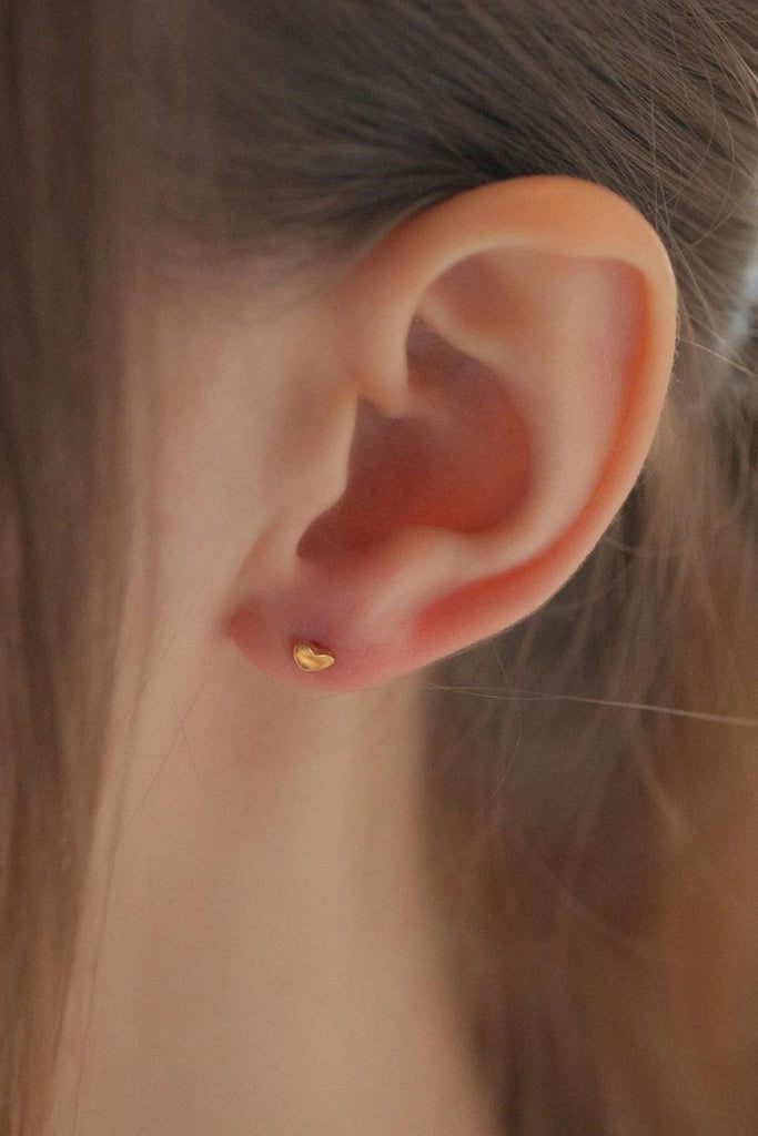 model wearing a dainty gold heart stud earring on the earlobe showing the delicate size of the earrings