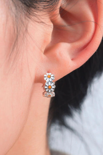 model wearing a sterling silver daisy chain hoop earring. the daisy flowers are white with a yellow centre, the outline of each flower is visible in silver