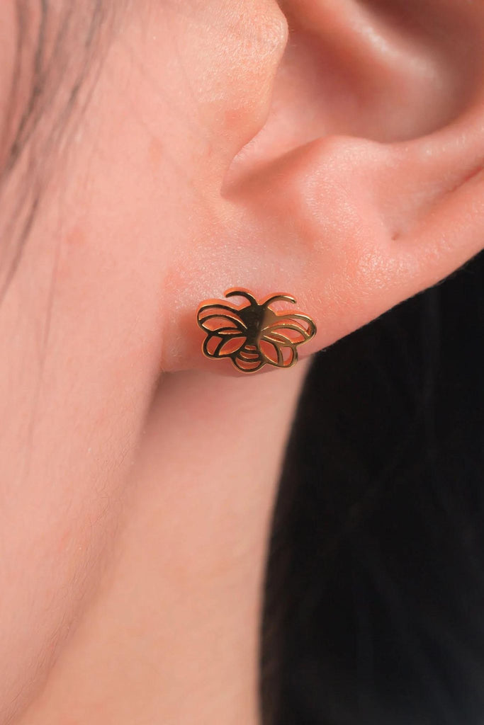 model wearing the gold openwork bee stud earring on the earlobe, showing the size of the earrings