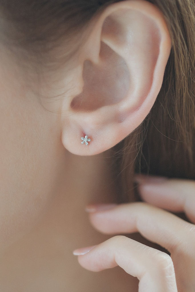 model wearing the silver dainty floral stud earring on the earlobe, showing the delicate size of the earrings