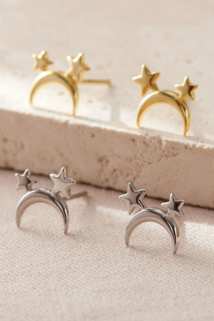 silver and gold coloured stud earrings, a crescent moon with two small stars attached to it