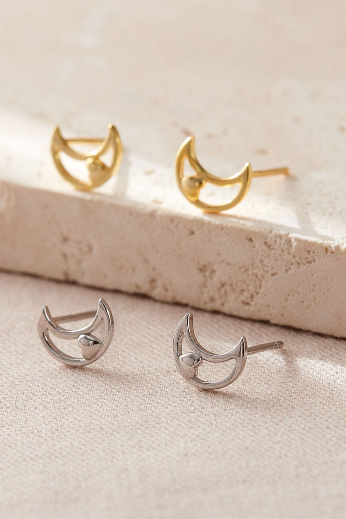 silver and gold coloured crescent moon stud earrings, the studs are openwork with a dainty solid love heart detail inside the crescent moon