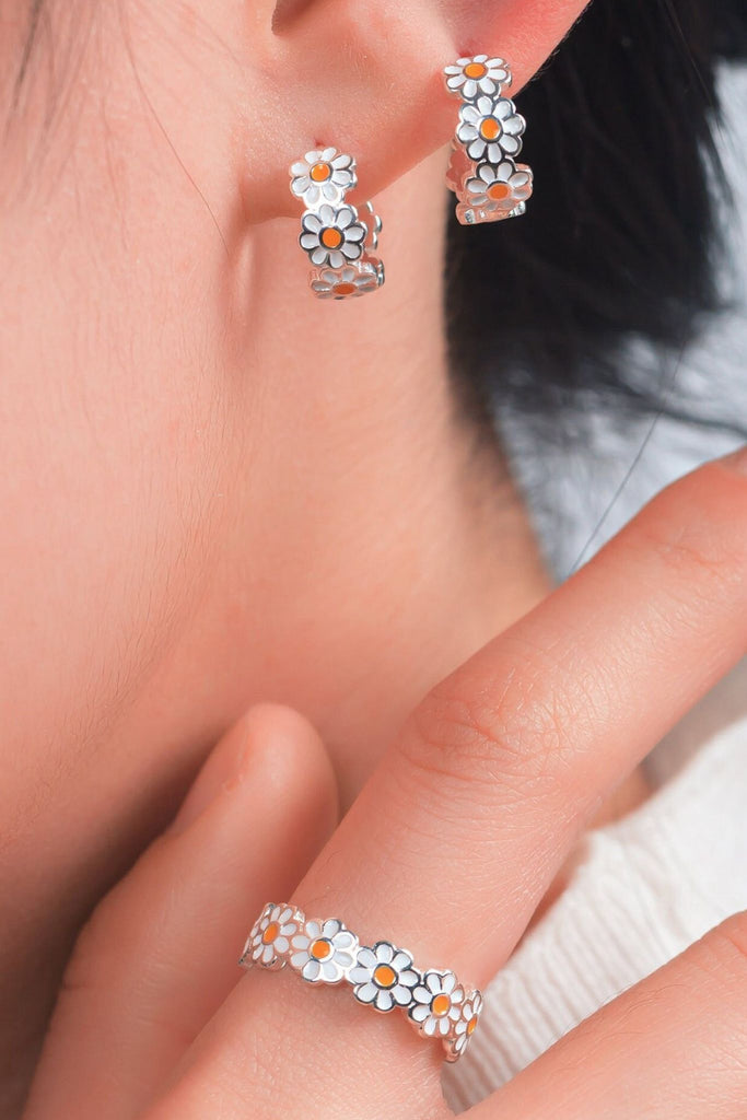 model wearing daisy flower hoop earrings and a matching ring, both made from sterling silver