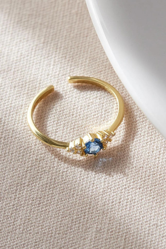 gold coloured open band sterling silver ring with a blue cz crystal centred in the middle, on either side of the blue crystal are three dainty white cz stones arranged like a pyramid