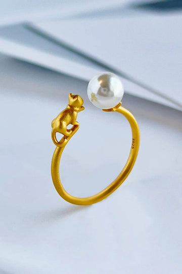 yellow gold plated sterling silver open band ring featuring a cat and a pearl, the cat and pearl are on opposite sides of the opening looking like the cat is pawing at the pearl ball