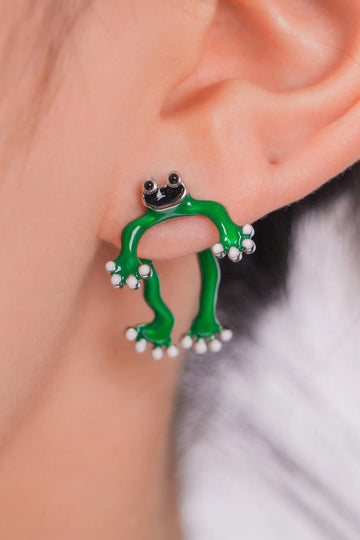 model wearing a green cartoon frog ear jacket, the front legs of the frog are on the outside of the earlobe, the back legs are on the back of the earlobe