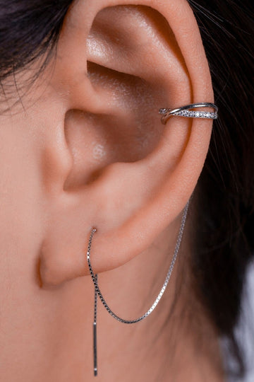 model wearing a sterling silver cross shaped clip on ear cuff  with a threader chain looping through an earlobe piercing. the cross shaped cuff has small white cubic zirconia crystals on them