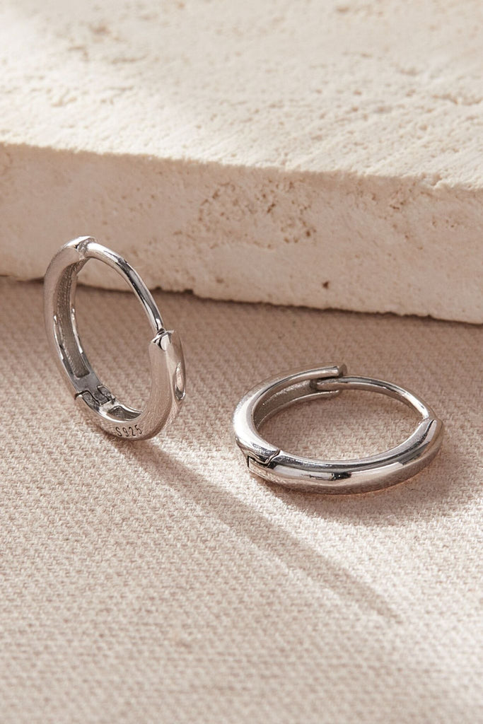 close up of the silver huggie hoop earrings, showing the s925 stamp and the latch hoop closure