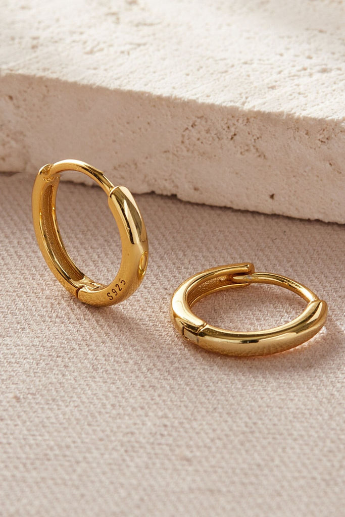 close up of the gold plated  silver huggie hoop earrings, showing the s925 stamp and the latch hoop closure