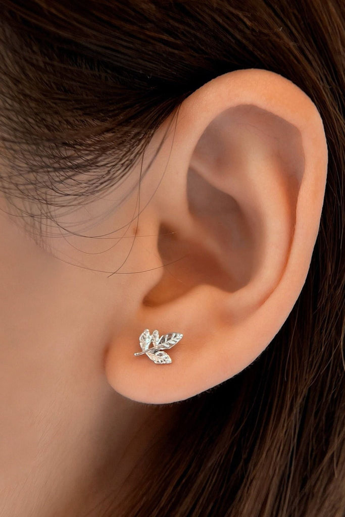 model wearing a small stud earring in the shape of a small bunch of leaves, the earring is made from S925 sterling silver and has a butterfly back