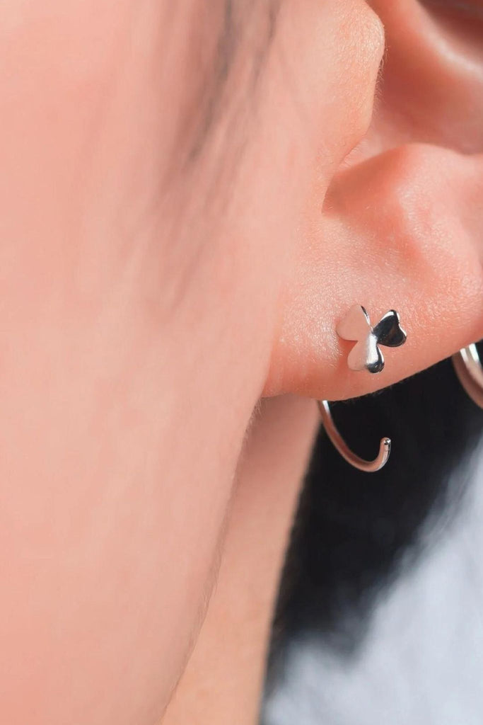 model wearing a silver shamrock hook earring, the hook goes through the earlobe and is secured in place by the shamrock