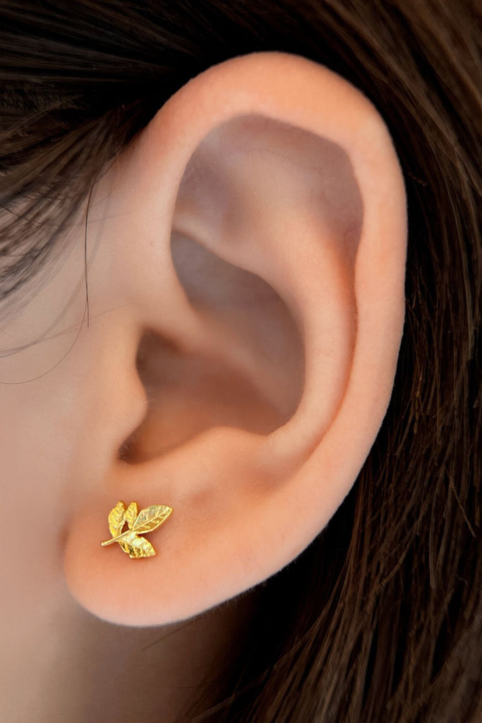 model wearing the gold coloured sterling silver leaves stud earrings, showing the dainty size of these studs