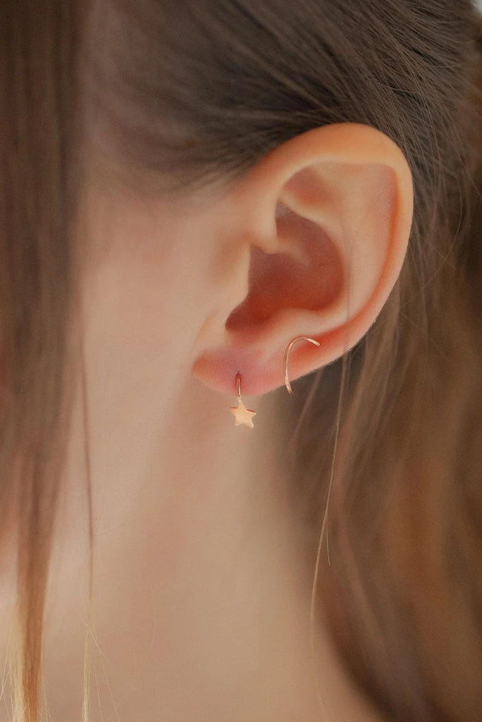 close up of a model wearing the rose gold spiral star earring, showing how the feed through the earlobe and spiral around the ear cuff