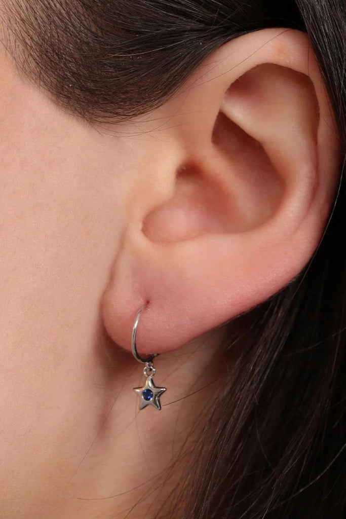 model wearing a small star dangle hoop earring with a blue cz middle, the star charm hangs below the earlobe