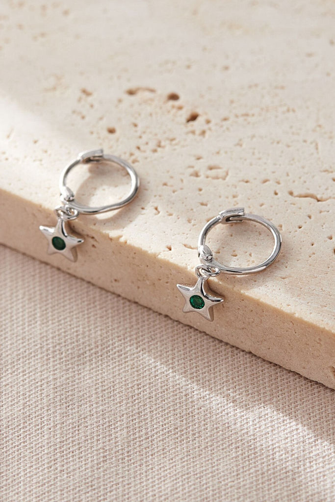 close up of the star charm hoop earrings, showing clearly colourful cz centres, these have green stones in the middle and represent the month of may