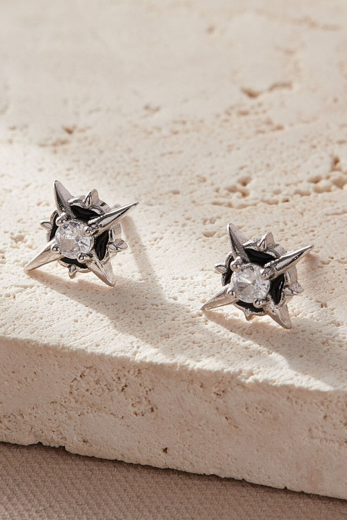 a pair of sterling silver starburst stud earrings with a large white cz crystal in the middle, the earrings are shaped like the north star ad have butterfly backs