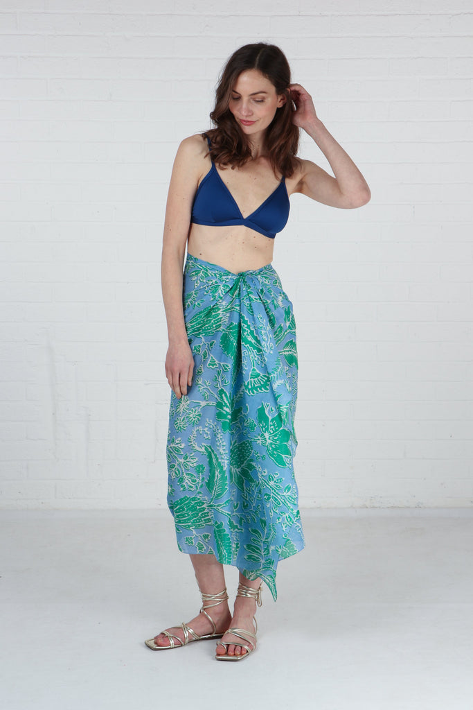 model wearing this blue and green floral cotton scarf tied around the waist and worn like a beach sarong