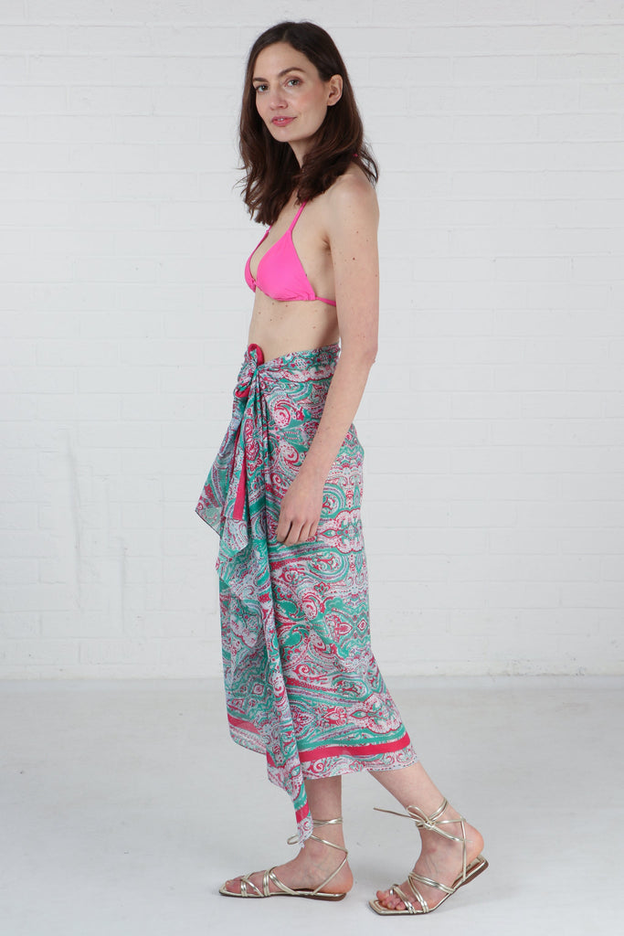 model wearing this green and pink paisley pattern scarf tied around the waist to show that it can be worn as a beach cover up sarong