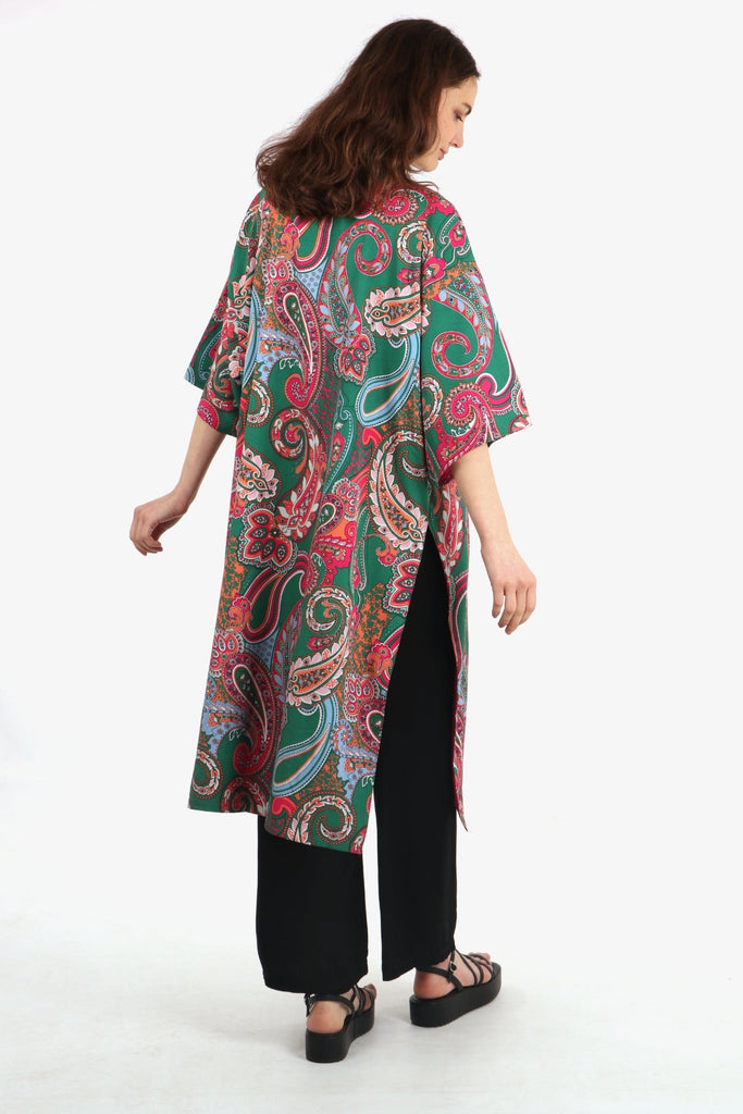 model showing the back of the kimono, showing an all over colourful paisley print patten in green and pink