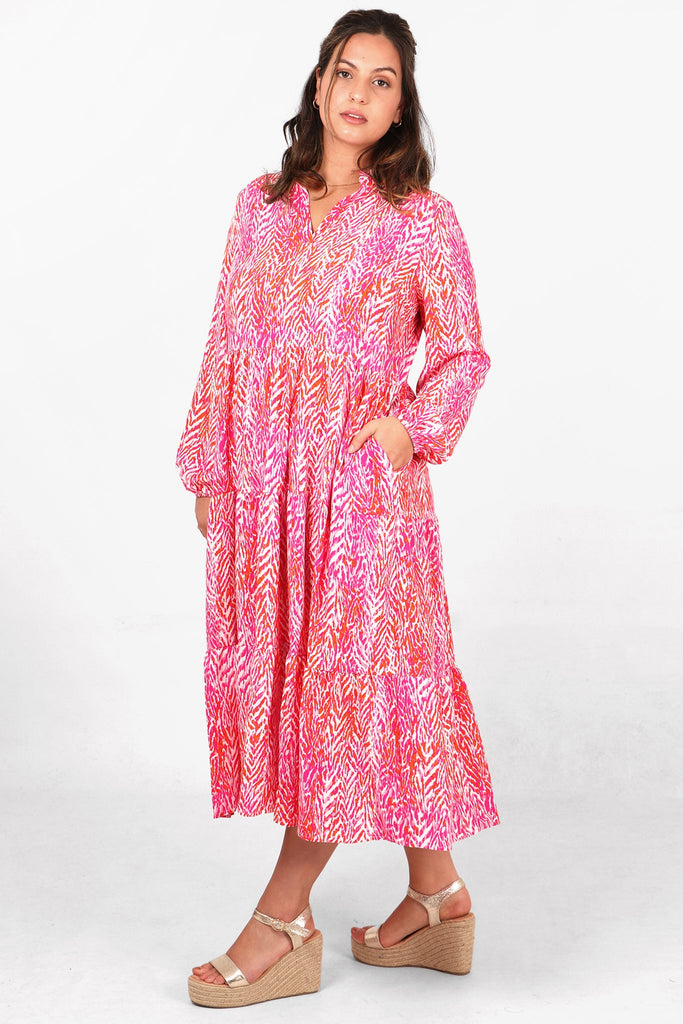 model wearing an abstract chevron print tiered midi dress with long sleeves, grandad collar and pockets