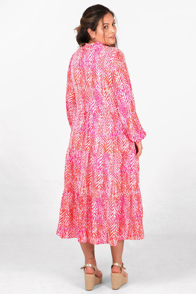 model showing the back of the pink tiered midi dress, showing an all over pattern 