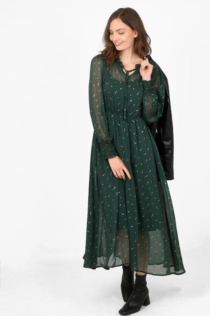 model wearing a bottle green chiffon dress with matching underlayer, the dress has an all over gold shooting star foil print pattern