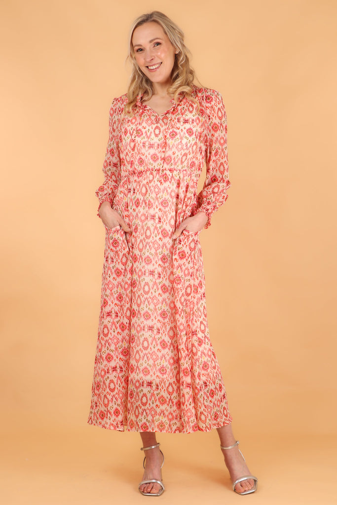 model wearing a midaxi length coral  aztec print long sleeve dress, the dress has pockets