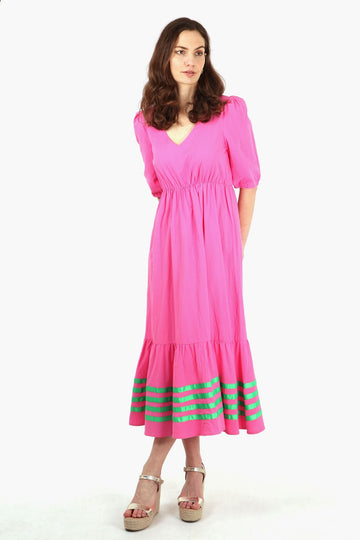 model wearing a pink midaxi length dress with four horizontal green ribbon stripes on the bottom tier of the dress, dress has a v neck and elbow length short sleeves