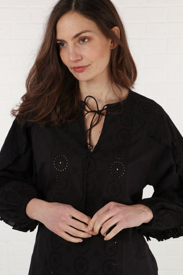 model wearing a black long sleeve cotton blouse with a grandad collar and a broderie anglaise detail on the front and sleeves