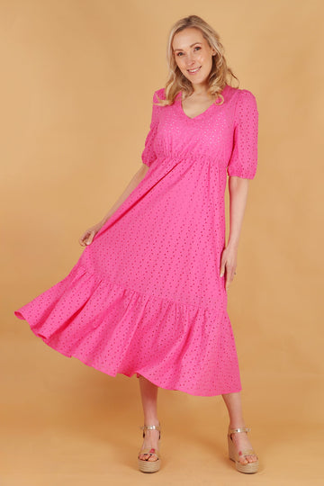 model wearing a plain pink tiered midaxi length dress with broderie anglaise details, short puff sleeves nad a v neck